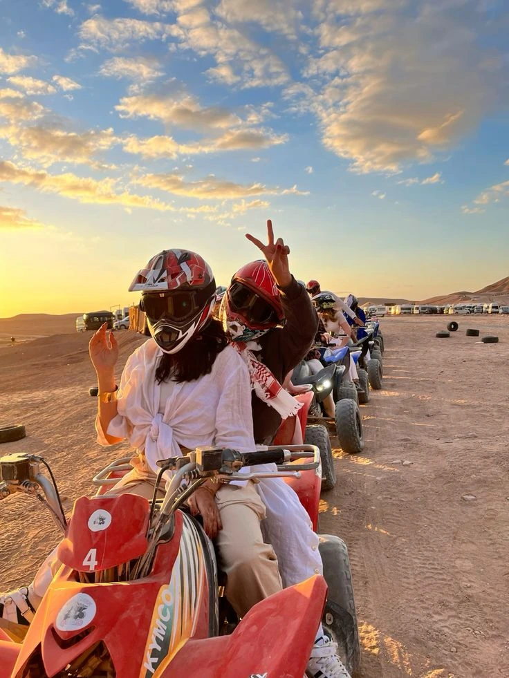sortie-quad-groupe-agafay-marrakech.webp Alt : Groupe de touristes en quad avec casques au coucher du soleil dans le désert d'Agafay