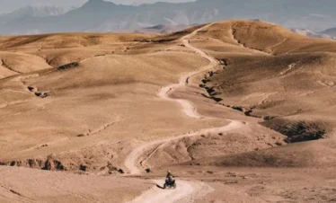 Deux quads sur une piste sinueuse à travers les collines du désert d'Agafay avec l'Atlas en arrière-plan